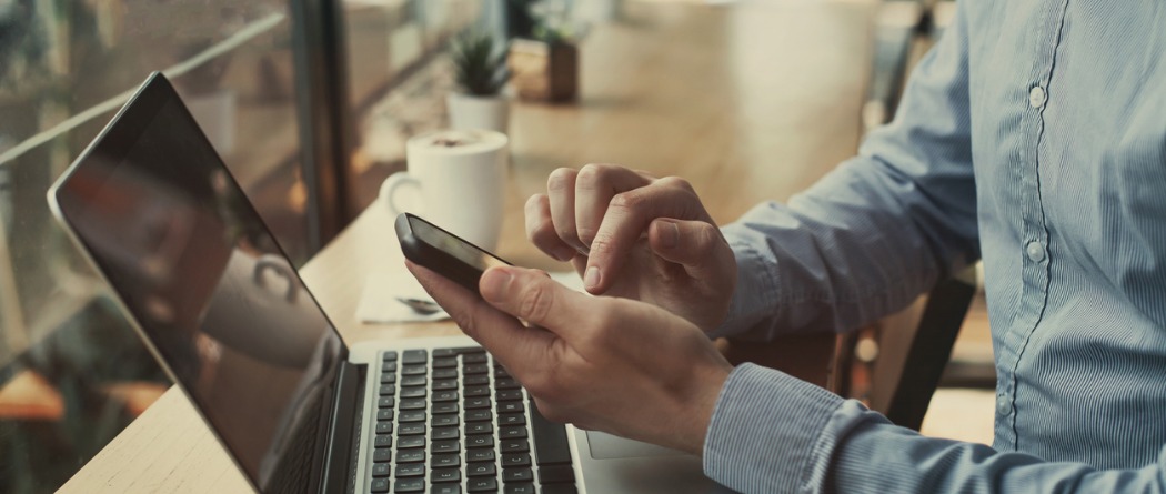 Person on their phone with a cup of coffee and an open laptop