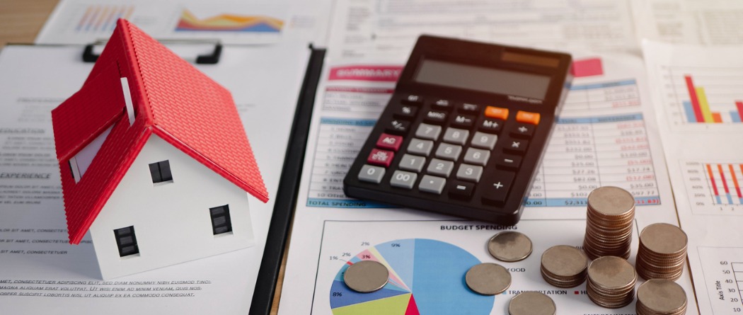 Calculator sitting on some paperwork with  a few coins and a toy house on the table