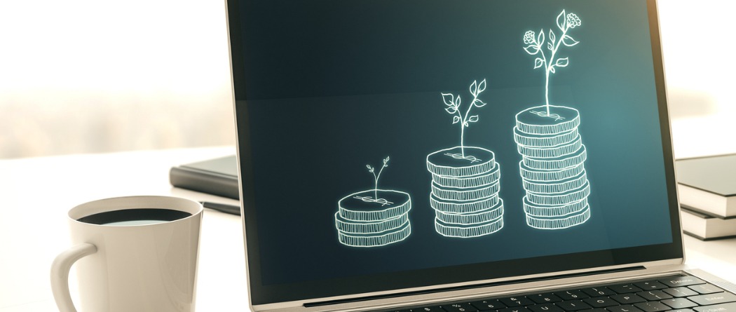 Laptop screen open showing varying increments of coins growing with a cup of coffee next to it